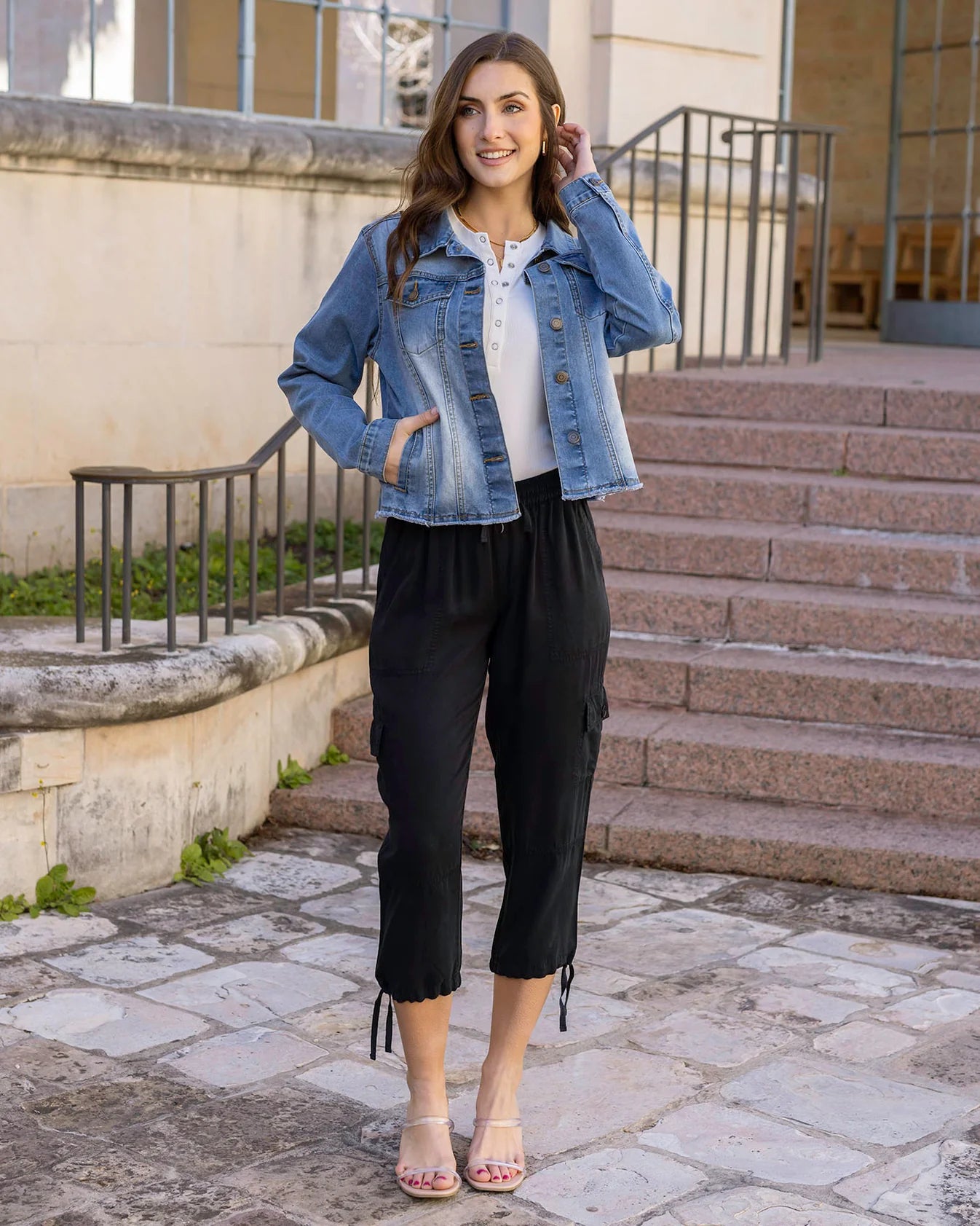 Woman wearing a denim jacket and black pants standing on stone steps outdoors.