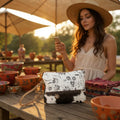 Woman using a phone with a floral-patterned clutch from Myra Bag sitting on a wooden table outdoors.