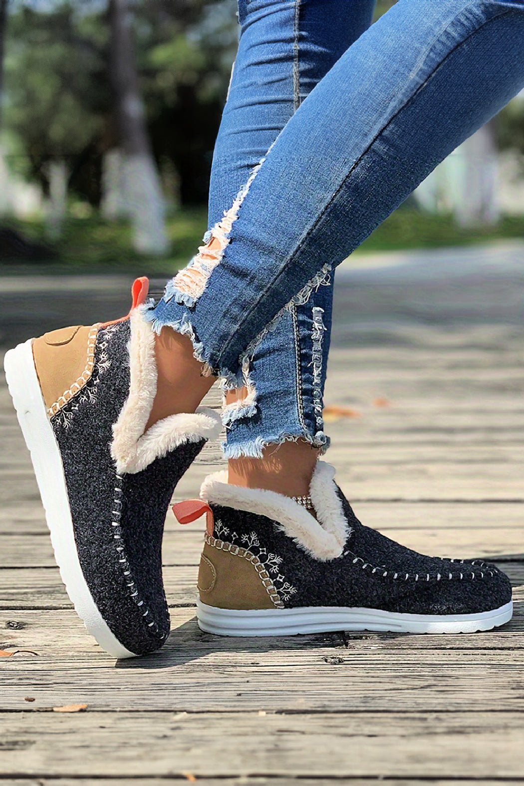 Grey and tan slippers with fur lining worn by a person on a wooden sidewalk.