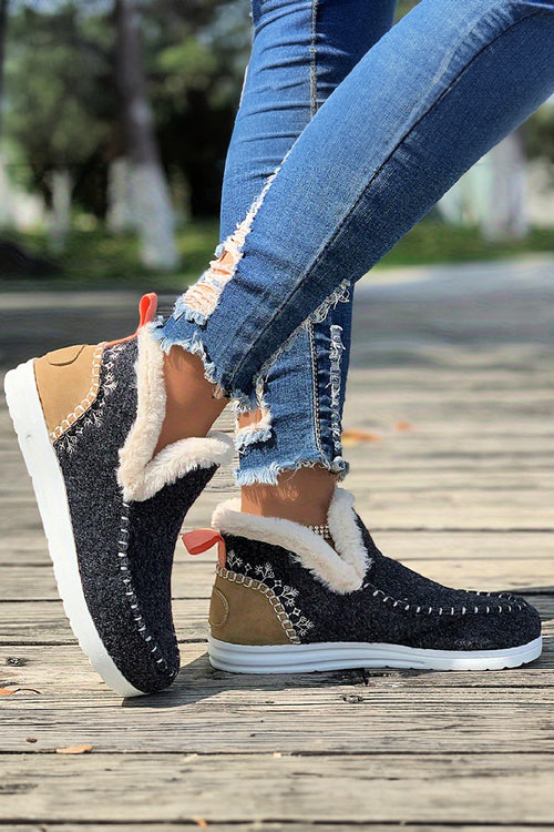 Grey and tan slippers with fur lining worn by a person on a wooden sidewalk.