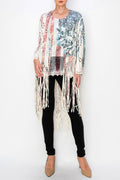 A model wearing a faux suede fringe jacket with a floral red, white and blue pattern. The jacket has long bell sleeves and fringe detailing at the hem.