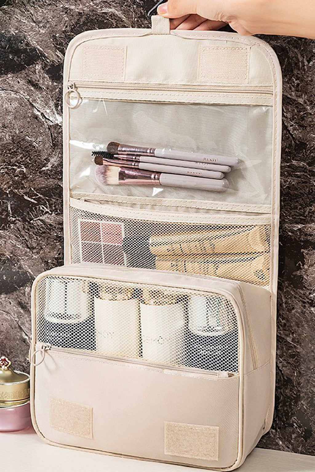 Beige travel makeup organizer with brushes and products against a marble background