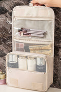 Beige travel makeup organizer with brushes and products against a marble background
