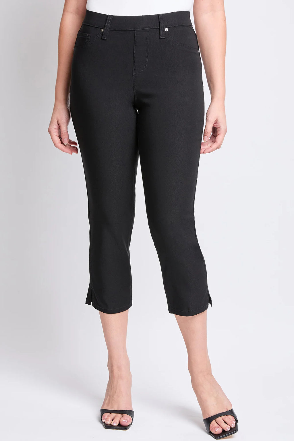 A pair of YMI junior hyperstretch pull-on capri pants in black with side slit, faux front pockets, and functioning back pockets.